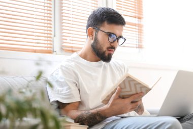 Evde sınava hazırlanan dizüstü bilgisayarı ve kitapları olan bir erkek öğrenci.