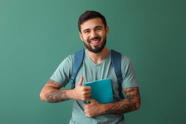 Handsome tattooed student showing thumb-up on green background