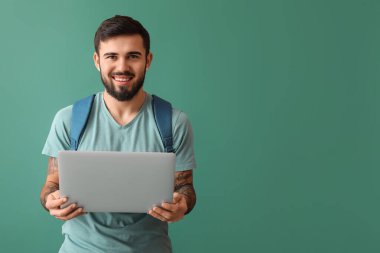 Handsome tattooed student with laptop on green background