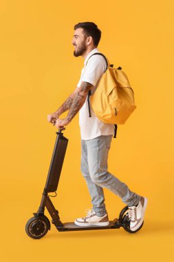 Handsome tattooed student with kick scooter on yellow background