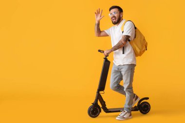 Handsome tattooed student with kick scooter on yellow background