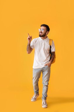 Handsome tattooed student pointing at something on yellow background
