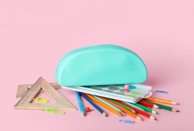 Blue pencil case with school stationery on pink background