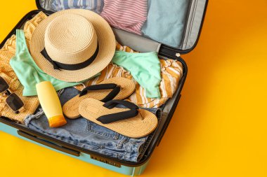 Open suitcase with beach accessories and clothes on color background, closeup