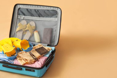 Open suitcase with clothes, passport and beach accessories on color background