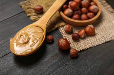 Spoon with hazelnut butter and plate of nuts on dark wooden background, closeup
