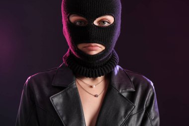 Young woman in balaclava and leather jacket against dark background