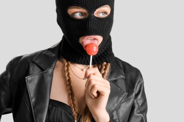 Young woman in balaclava with lollipop on light background