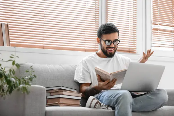 Evde sınava hazırlanan dizüstü bilgisayarı ve kitapları olan bir erkek öğrenci.