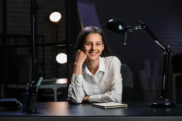 Smiling businesswoman sitting in office at night