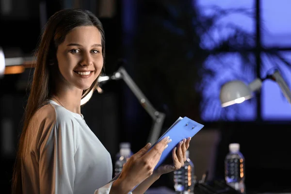 Smiling businesswoman with clipboard in office at night