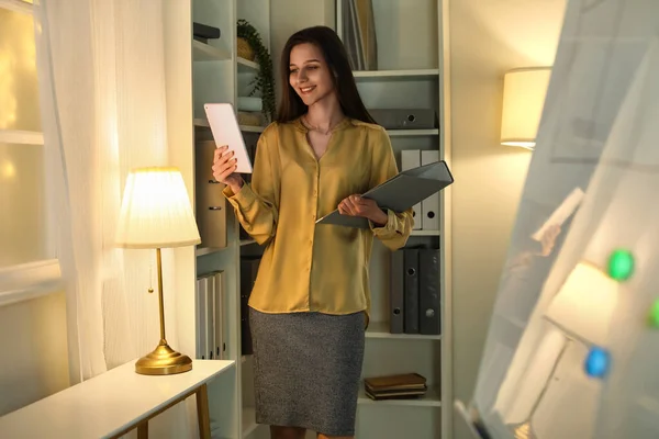 Beautiful businesswoman with tablet computer and folder late in evening