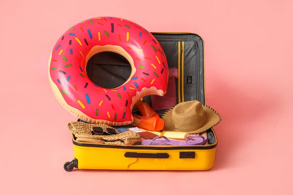 Open suitcase with clothes, different beach accessories and passport on pink background