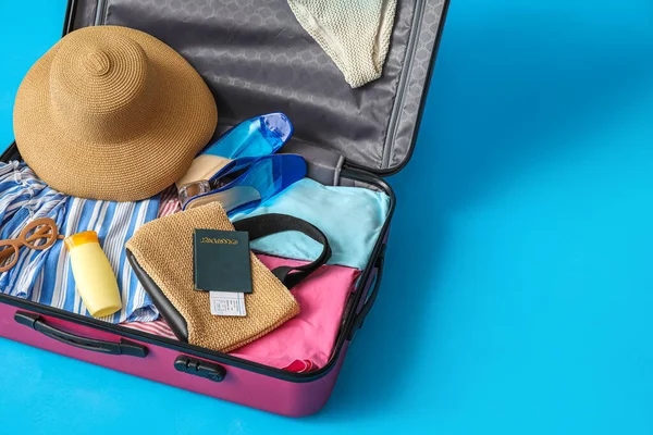 Open suitcase, beach accessories, ticket and passport on blue background