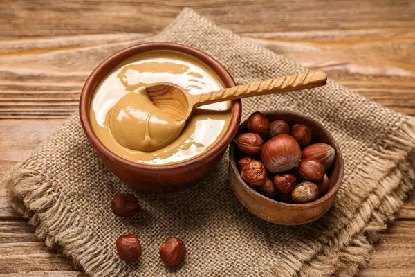 Bowls of tasty hazelnut butter and nuts on wooden background