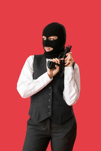 Young woman in balaclava with gun against red background