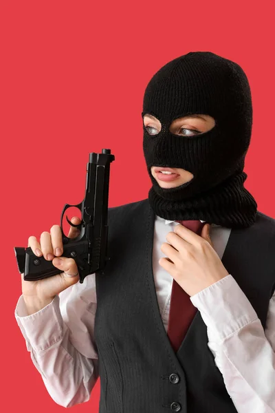 Portrait of young woman in balaclava with gun against red background
