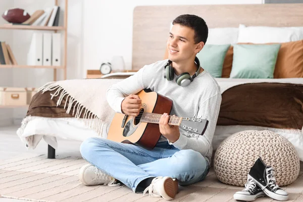 Teenage boy playing guitar in bedroom