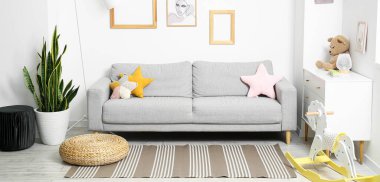 Interior of light room with sofa, carpet, chest of drawers and child's toys