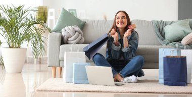 Happy young woman with laptop, credit card and many shopping bags at home
