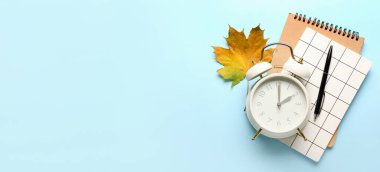 Alarm clock, notebooks and autumn leaf on light blue background with space for text