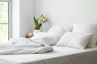 Wilted houseplant, lamp and cup of coffee on table near light wall in bedroom
