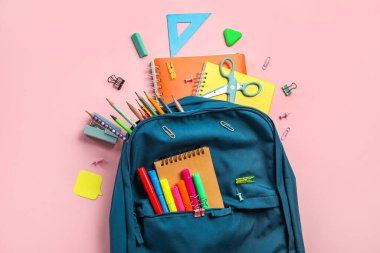 School backpack with stationery supplies on pink background