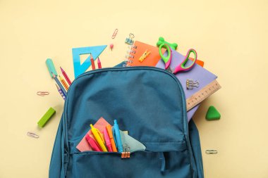 Blue backpack with school stationery on beige background