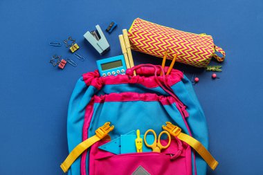 School backpack with stationery on blue background
