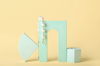 Showcase pedestal with stylish pearl jewelry on color background