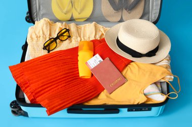 Suitcase with clothes, passport, ticket and beach accessories on color background, closeup