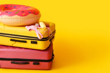 Suitcases with bottle of sunscreen, bikini bra, passports, tickets and inflatable ring on yellow background
