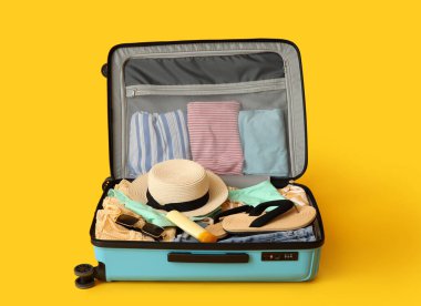 Open suitcase with beach accessories and clothes on color background