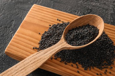 Wooden board with spoon of black sesame seeds on dark background, closeup