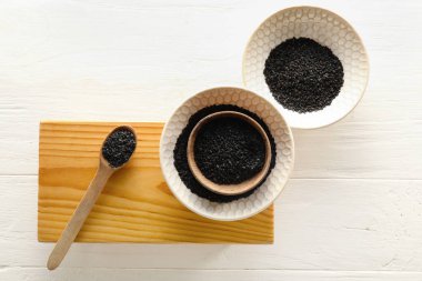Bowls with black sesame seeds on light wooden background