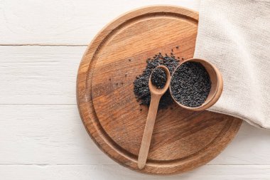 Board with bowl and spoon of black sesame on light wooden background