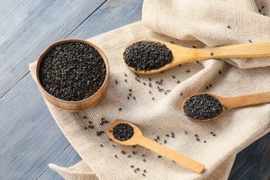 Bowl and spoons with black sesame seeds on dark wooden background, closeup