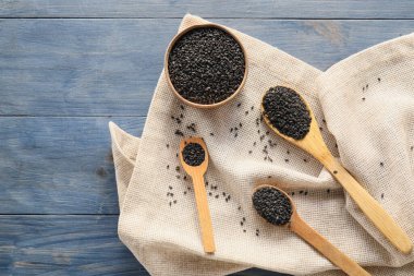Composition with bowl and spoons of black sesame seeds on dark wooden background