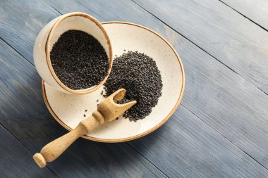 Plate with bowl and scoop of black sesame seeds on dark wooden background