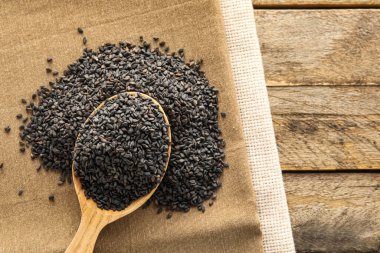 Spoon with black sesame seeds on wooden table, closeup