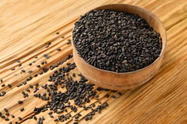 Bowl of black sesame seeds on wooden background, closeup