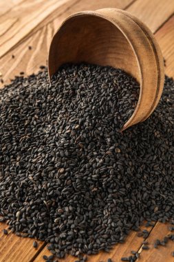Overturned bowl of black sesame seeds on wooden table, closeup