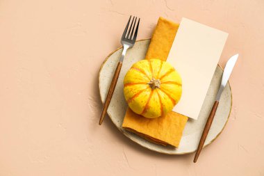 Table setting with pumpkin and blank card on beige background