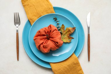 Table setting with autumn decor and pumpkin made of napkin on light background