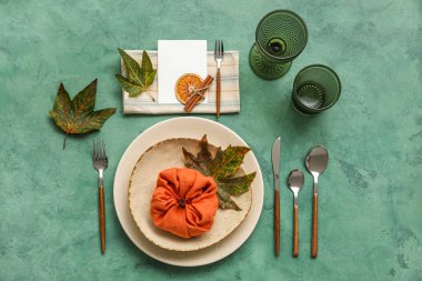 Stylish table setting with autumn leaves and pumpkin made of napkin on green background