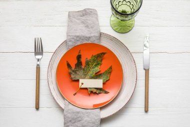 Table setting with autumn leaf and blank card on white wooden background