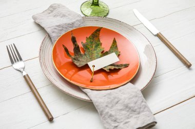 Autumn leaf and blank card on white wooden table