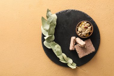 Board of tasty sesame halva with pistachios and eucalyptus branch on color background