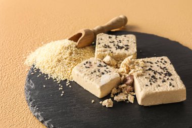 Slate board with pieces of tasty sesame halva on color background, closeup