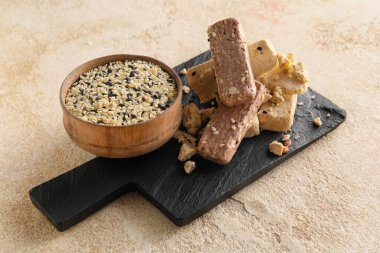 Board with bowl of sesame seeds and halva on light background